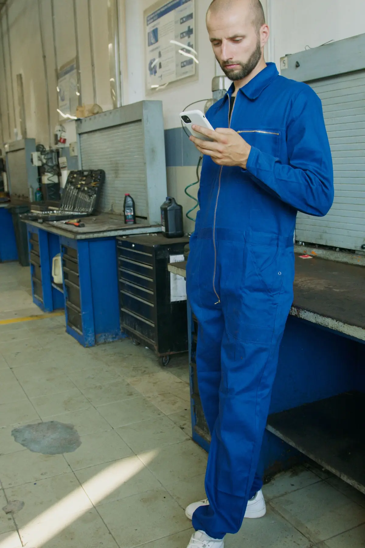 Mechanic in blue overalls reading a phone in a workshop